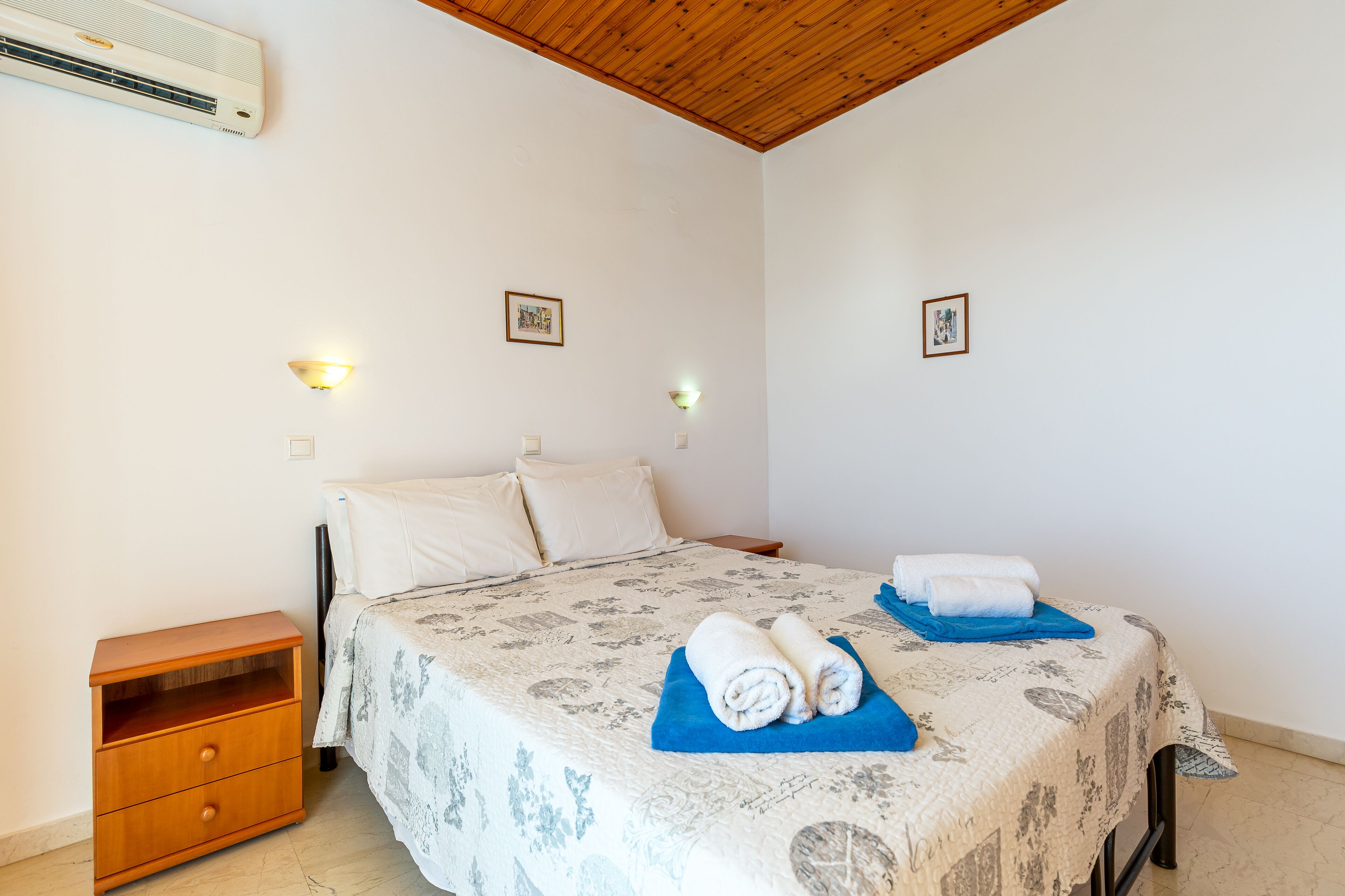 A bedroom with a bed, a nightstand, a wall-mounted air conditioner, and two wall-mounted light fixtures.