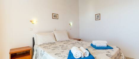 A bedroom with a bed, a nightstand, a wall-mounted air conditioner, and two wall-mounted light fixtures.