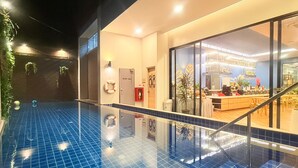 An indoor swimming pool with a tiled floor, a lifebuoy on the wall, and a bar area visible through a glass partition. - Golden Paradise Hotel (Karon)