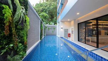 A modern hotel interior with a blue tiled pool, indoor plants, and a contemporary dining area.