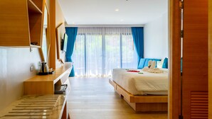 A modern hotel room with a wooden bed, a desk with a chair, and a large window with curtains. - Golden Paradise Hotel (Karon)