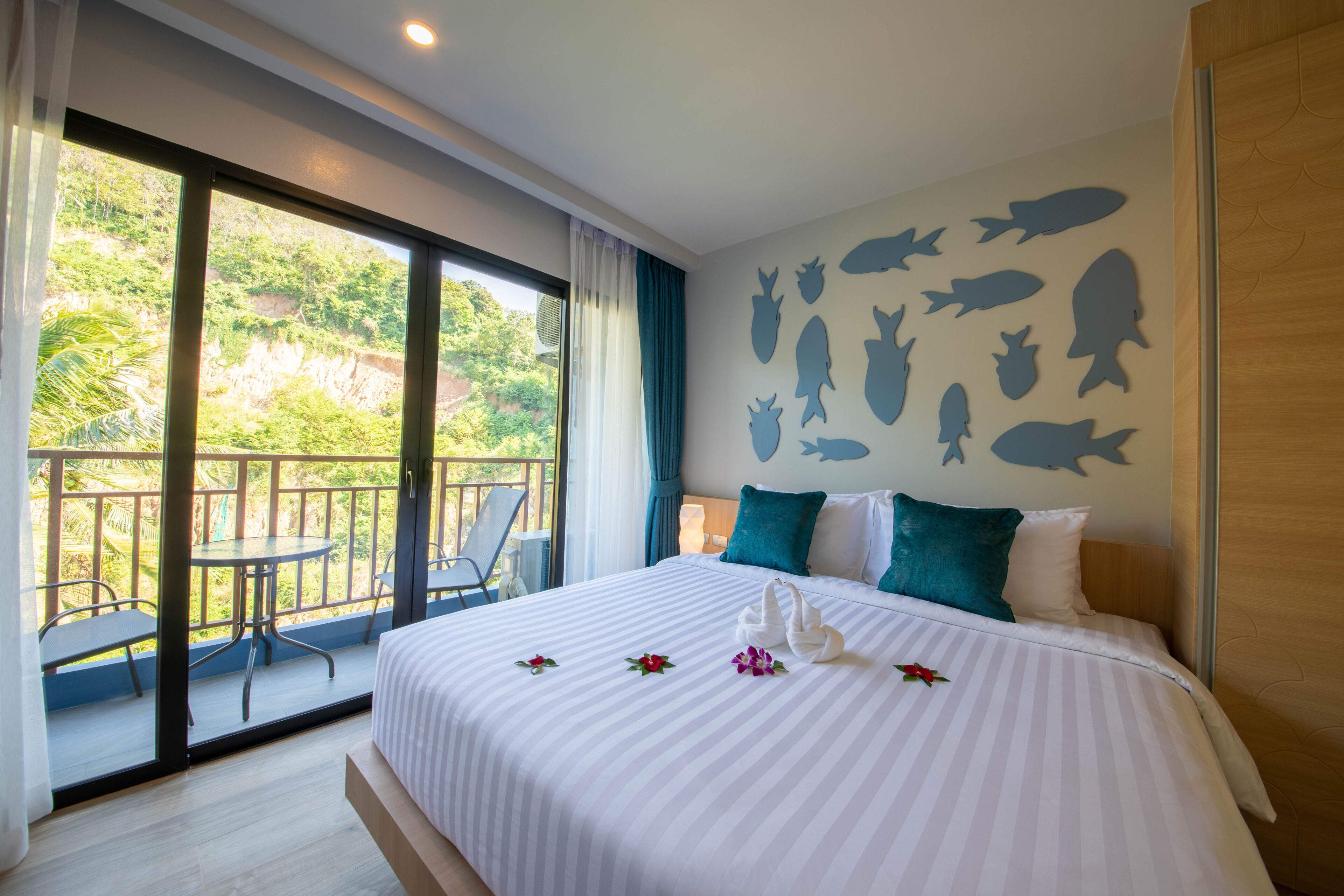 Habitación de hotel con una cama grande, un balcón con sillas y una pared decorada con siluetas de peces.
