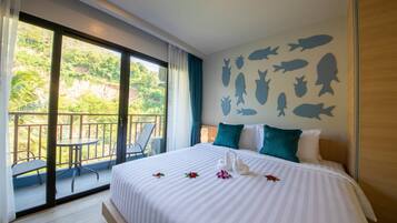 Habitación de hotel con una cama grande, un balcón con sillas y una pared decorada con siluetas de peces.
