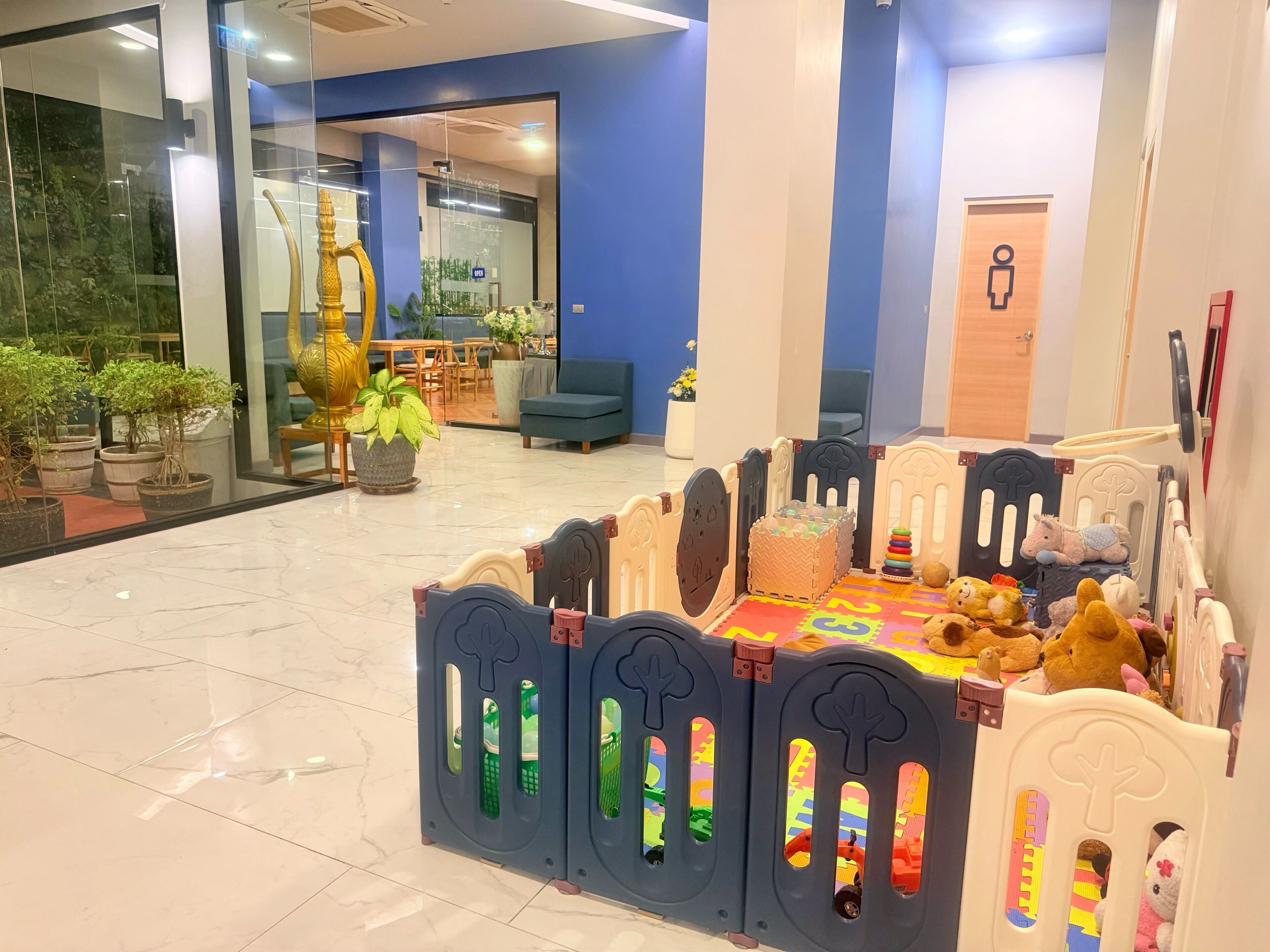A children's play area with a playpen, toys, and potted plants.