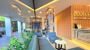 A modern hotel lobby with seating areas, a reception desk, and a glass partition. - Golden Paradise Hotel (Karon)
