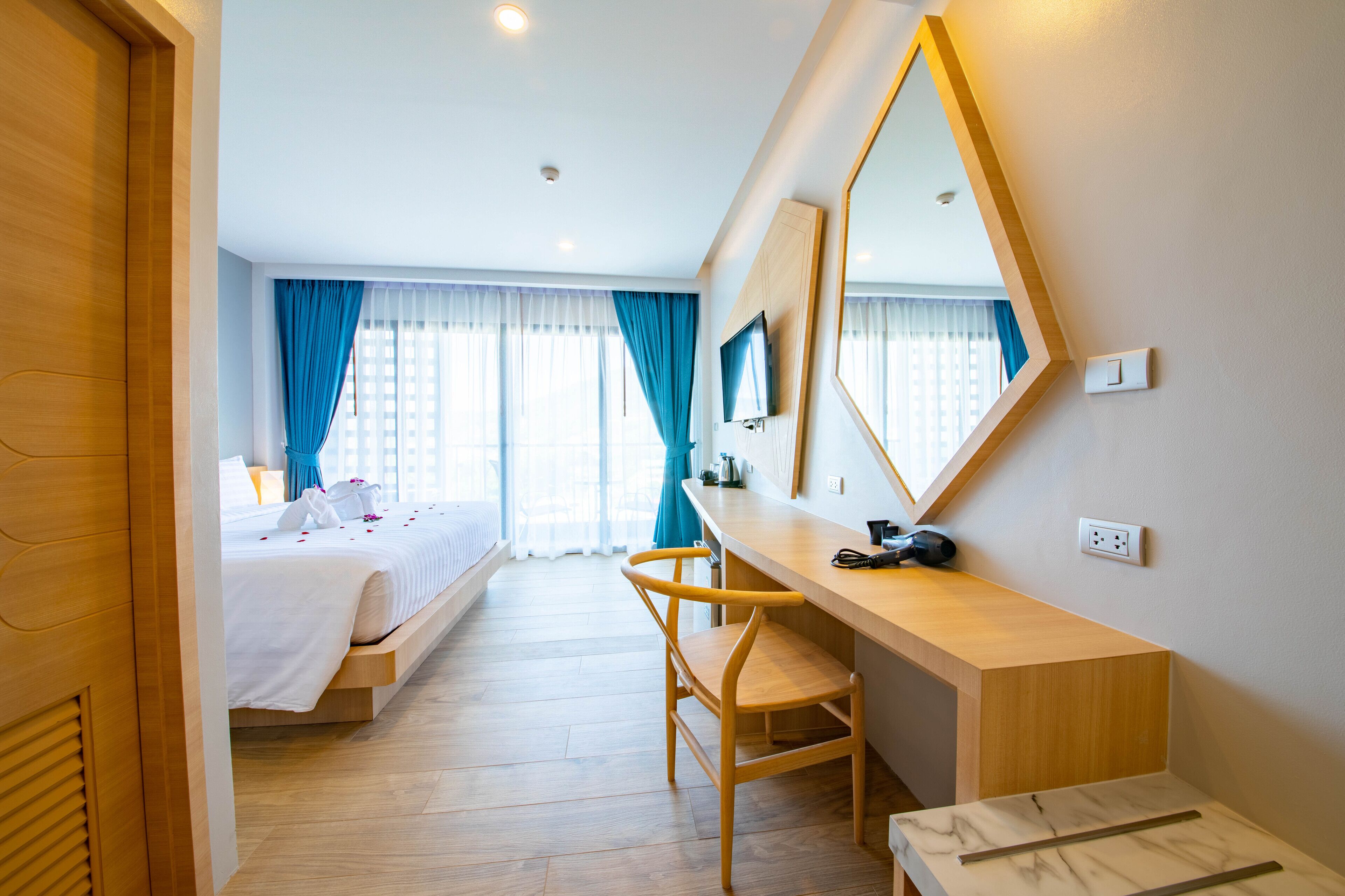 Habitación de hotel con cama, escritorio, silla, espejo y ventana con cortinas.