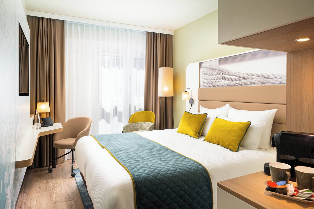 Habitación de hotel con cama, escritorio, silla, cafetera y bandeja con alimentos para el desayuno.