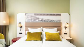 Ein Hotelzimmer mit einem großen Bett, zwei Nachttischlampen, einem Kopfteil mit einem Gemälde und einem roten Beistelltisch.
