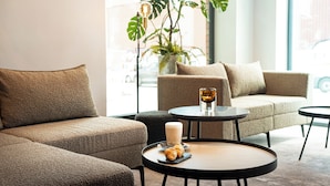A modern lounge area with a sofa, two round tables, a candle, and a croissant. - Leonardo Hotel Hamburg Altona (Hamburg)
