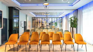 Un salón de conferencias con diseño moderno, que incluye un panel de vidrio, una planta grande y una fila de sillas naranjas.