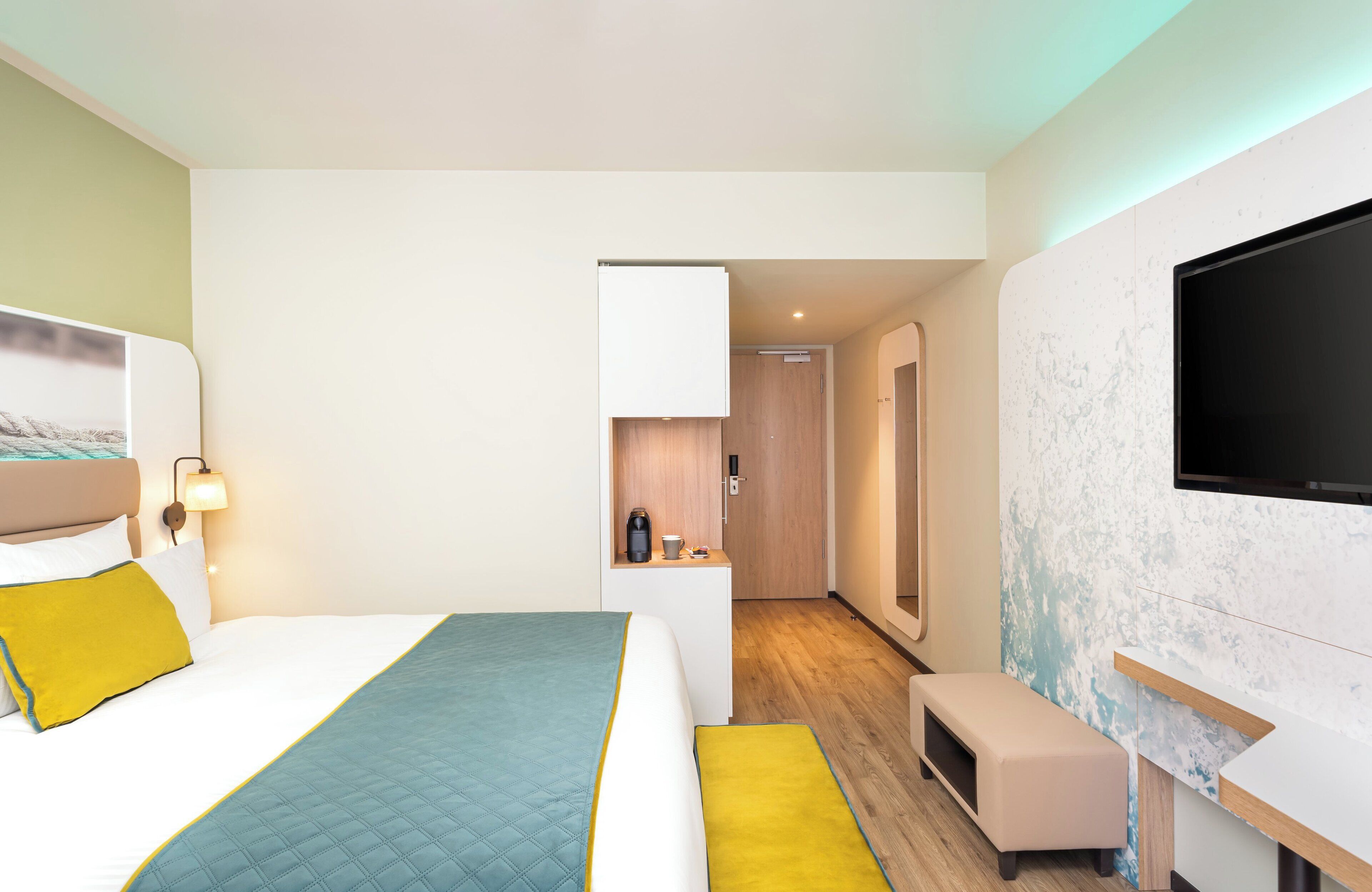 Una habitación de hotel moderna con una cama, mesita de noche, televisor y un pequeño rincón de descanso.