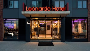 The exterior of the Leonardo Hotel with a modern design, large glass entrance, and a visible bar area inside. - Leonardo Hotel Hamburg Altona (Hamburg)