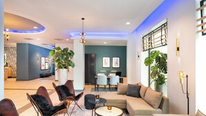 A modern hotel lobby with a sectional sofa, leather armchairs, a coffee table, and a dining area with a table and chairs. - Leonardo Hotel Hamburg Altona (Hamburg)