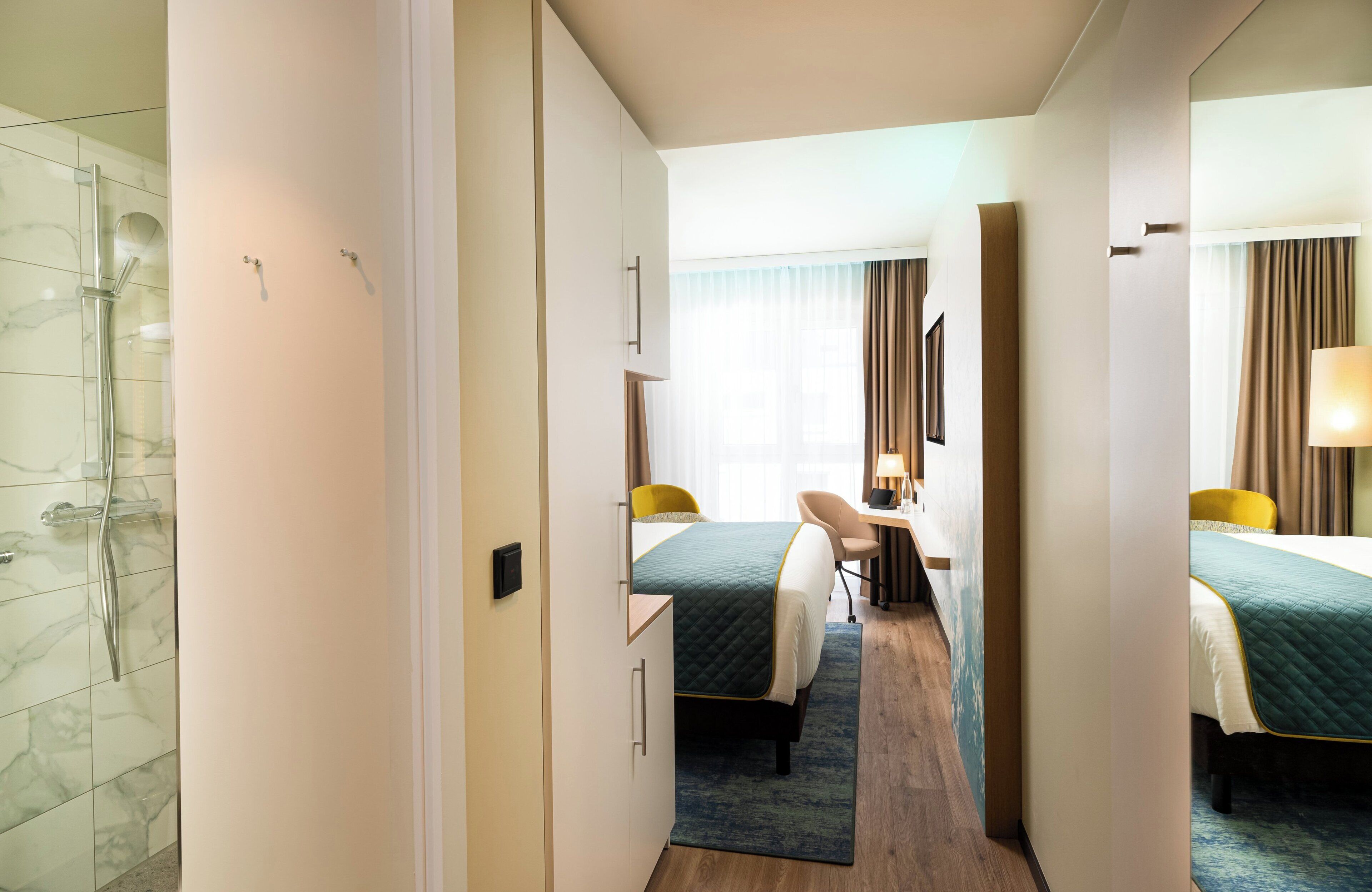 A hotel room with a shower, two beds, a desk, and a chair.
