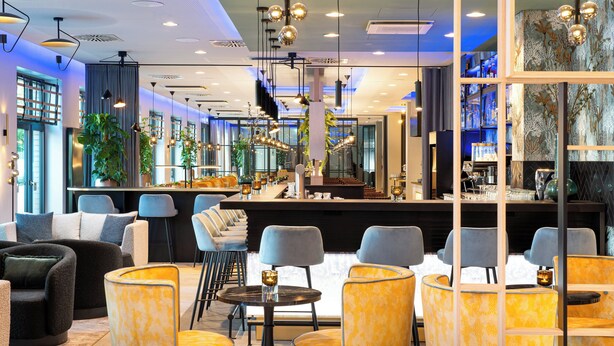 A modern bar area with seating, bar counter, and decorative lighting. - Leonardo Hotel Hamburg Altona (Hamburg)