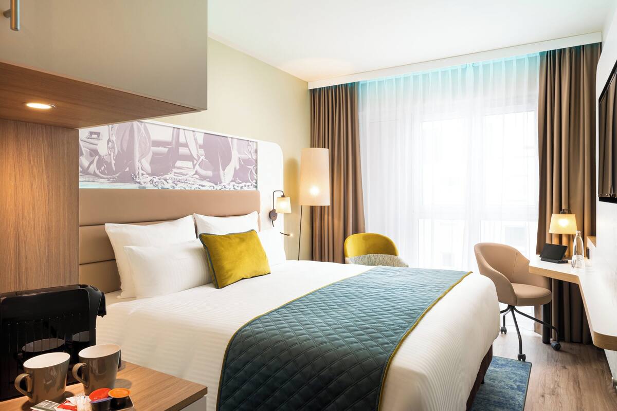 Una habitación de hotel con una cama grande, un escritorio con una computadora portátil, una cafetera y una silla.