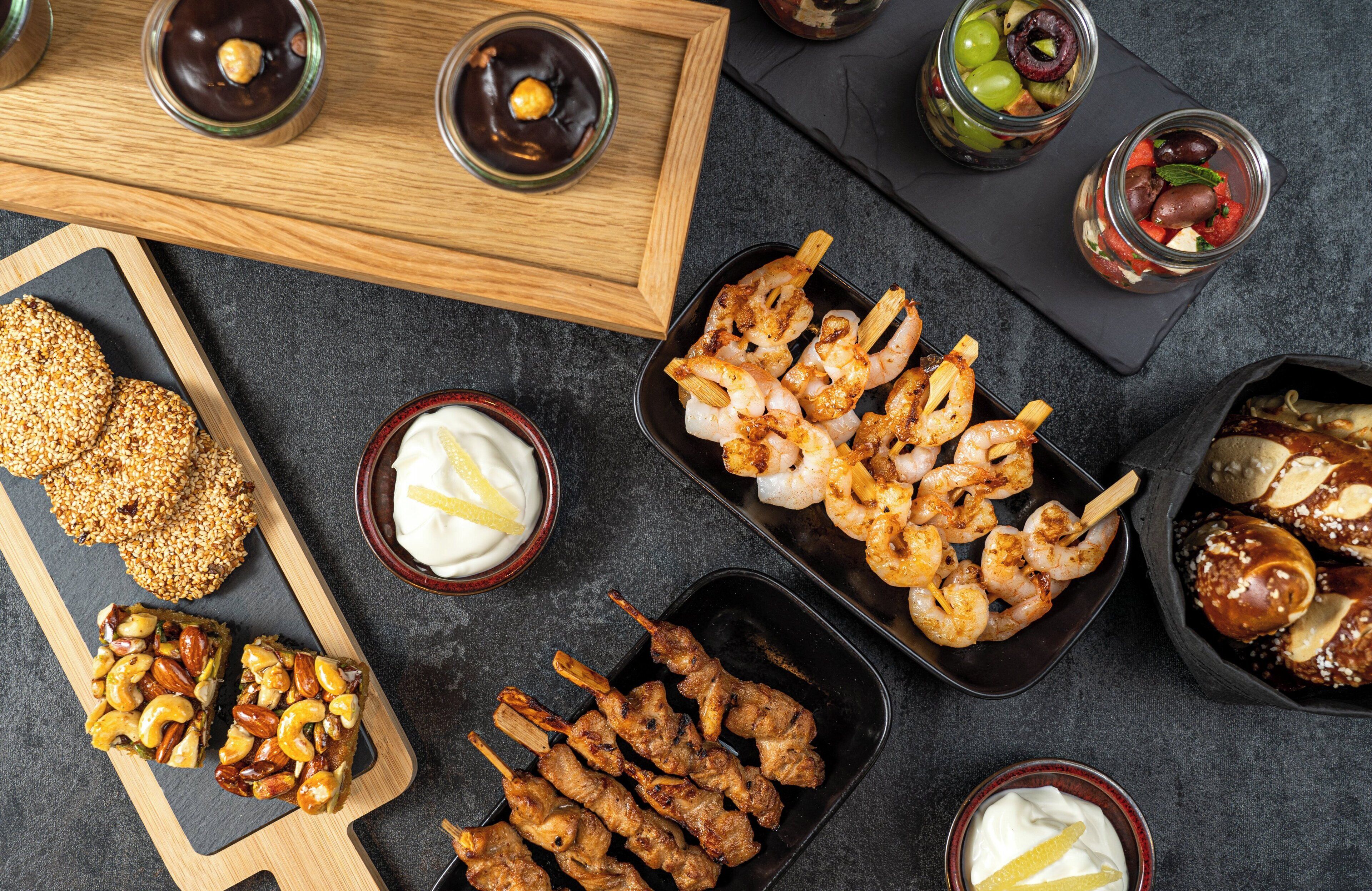 A variety of food items including shrimp skewers, meat skewers, and a dessert bar on a wooden board.