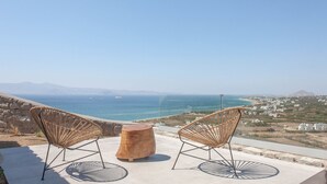 Una terrazza con due poltrone in vimini e uno sgabello di legno, affacciata su un paesaggio costiero.