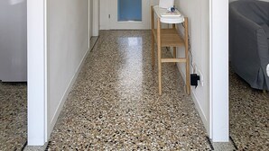 Un couloir étroit, avec un coin cuisine sur la gauche, un évier avec un miroir sur la droite, et une porte au fond.