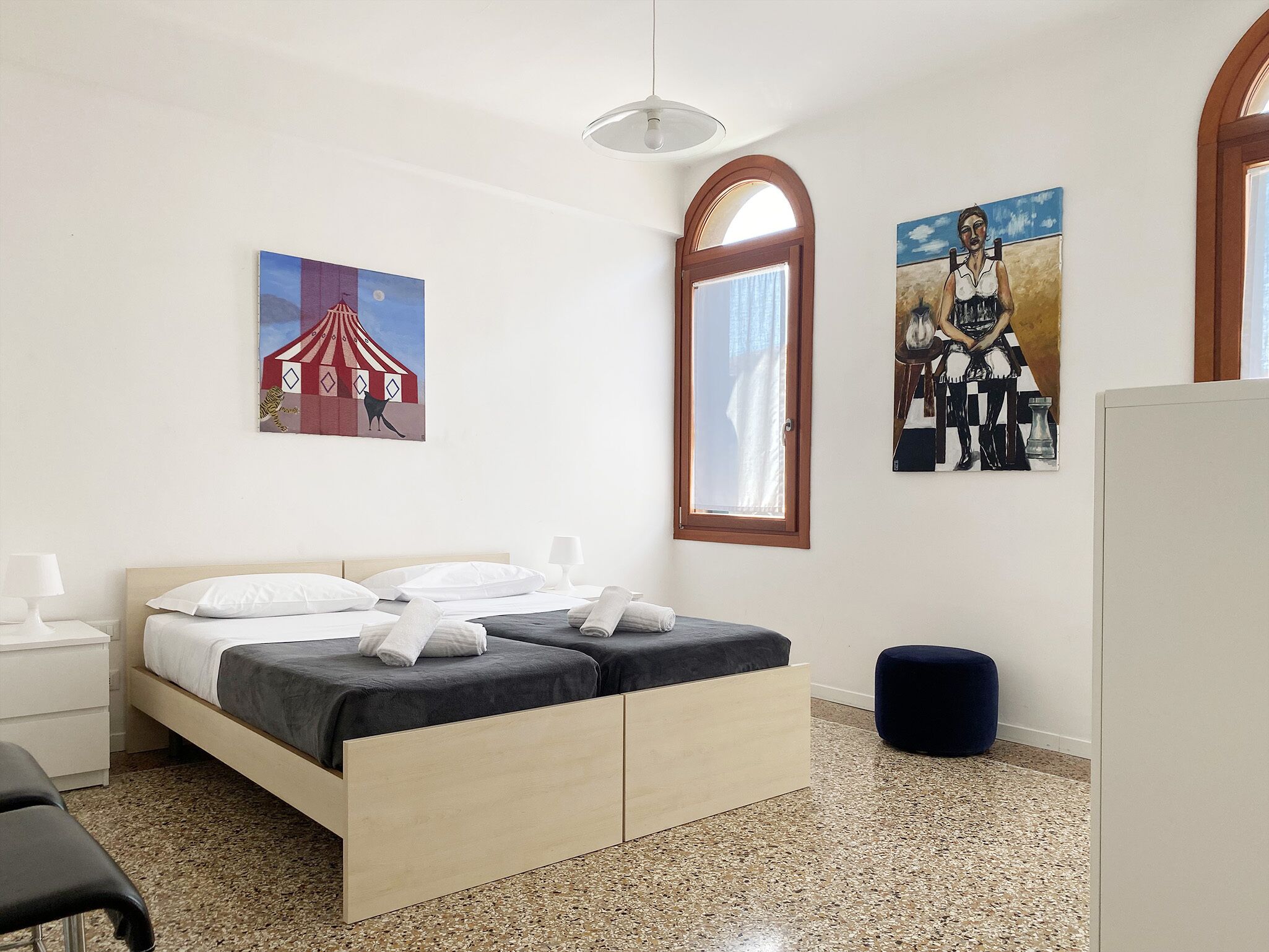 Een hotelkamer met een bed, een bureau, een stoel, een raam en twee schilderijen aan de muur.