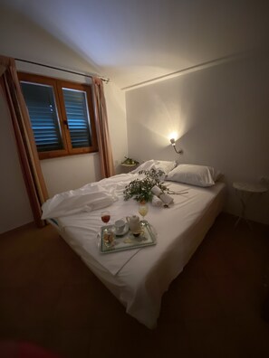 Una cama bien hecha con una bandeja de desayuno, una mesita de noche con una lámpara y una ventana con cortinas.