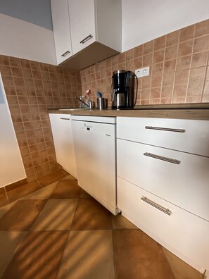Una cocina con gabinetes blancos, cafetera y lavavajillas.