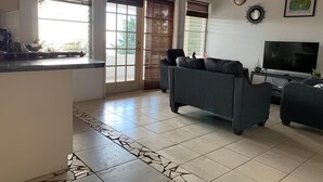 A living room with a sofa, a TV, and a kitchen area with a counter and a window.