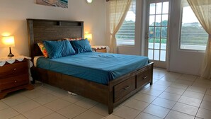 A bedroom with a wooden bed, two bedside tables with lamps, a window with curtains, and a painting on the wall.