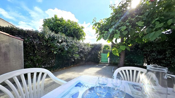 An outdoor patio with a table set for two, two wine glasses, and a pitcher.
