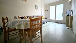 A dining area with a table, chairs, and a sofa. There is a television on a stand and a door leading outside.