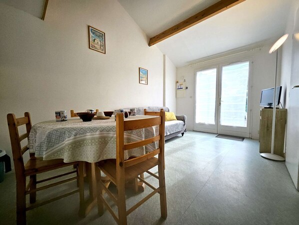 Ein Essbereich mit Tisch, Stühlen und einer Couch. Ein Fernseher steht auf einem Schrank und eine Tür führt nach draußen.