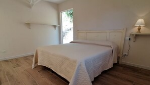 Un dormitorio con cama, suelo de madera, una lámpara de pared y una puerta que da al exterior.