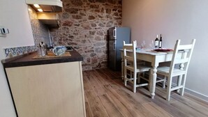 Una cocina compacta con pared de piedra, un refrigerador, una mesa de comedor con sillas y una pequeña isla con un lavamanos y una tetera.