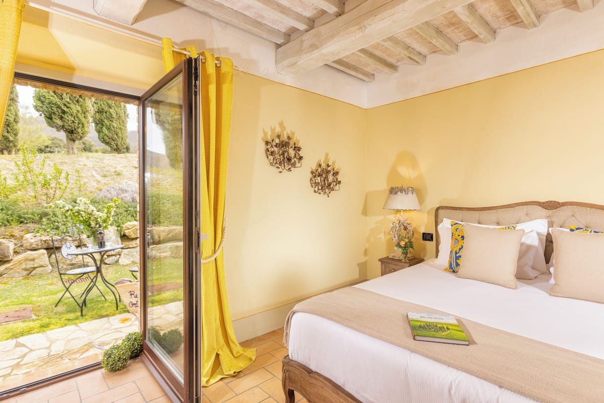 Un dormitorio con cama, mesita de noche, lámpara y vista a un jardín exterior a través de un ventanal.