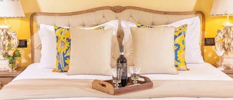 A neatly made bed with a wooden headboard, two decorative lamps, and a tray with a bottle and glasses.