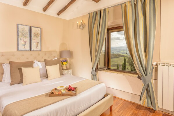 A bedroom with a bed, a nightstand, a lamp, a window with curtains, and a view of the countryside.
