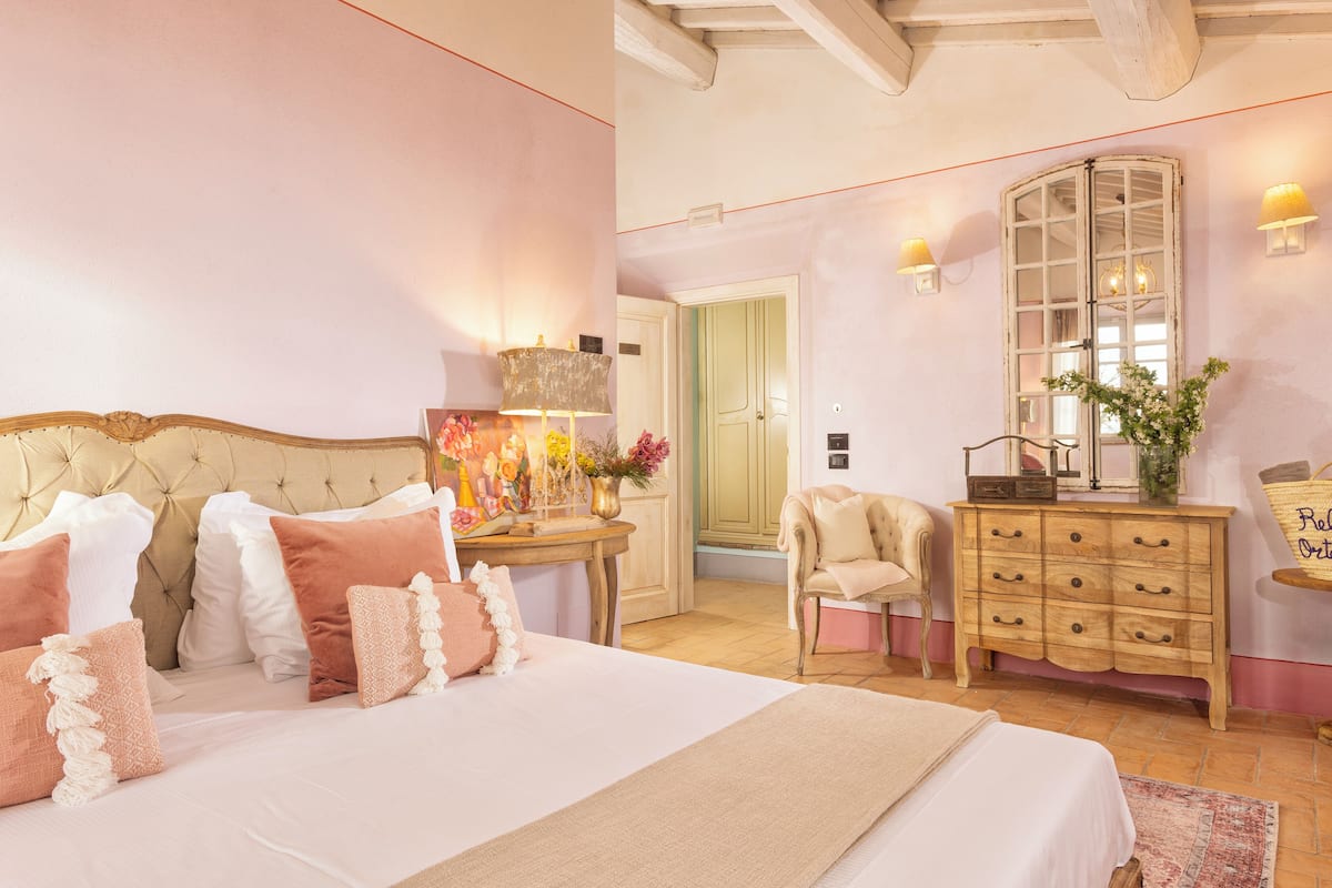 Un dormitorio con una cama grande, un aparador de madera, una silla y una mesa con lámpara.