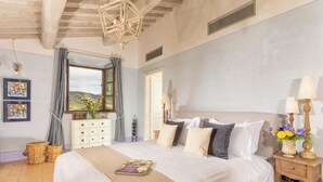 A bedroom with a large bed, a dresser, a nightstand with a lamp, and a window with a view of the outdoors. - Podere Val D'Orcia - Tuscany Equestrian (Sarteano)