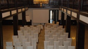 Une salle de conférence avec des rangées de chaises blanches, un grand écran et un lustre.