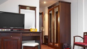 Une chambre d’hôtel avec un bureau en bois, une télévision, un miroir, une armoire, une chaise et une poubelle.