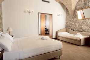 A bedroom with a large bed, a smaller sofa, a mirror, and a stone wall. - Giotto B&B (Assisi)