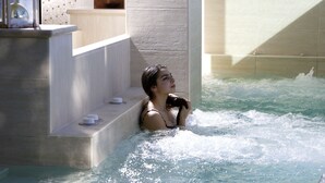 Iemand in een bubbelbad met een betegelde muur en een klein plankje met bekers.