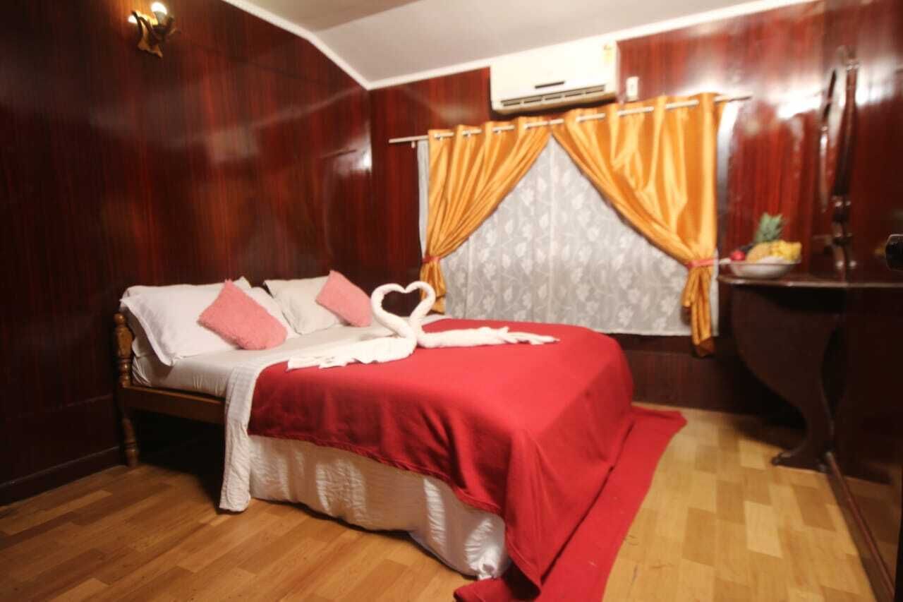 Une chambre avec un lit en bois, une couvre-lit rouge et un oreiller blanc orné d’un motif en forme de cœur.