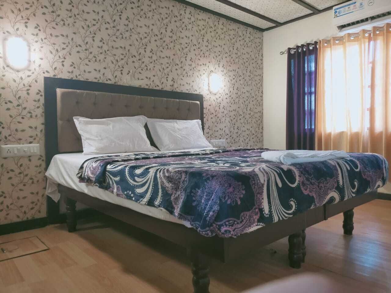 A bedroom with a bed, floral wallpaper, and a window with curtains.
