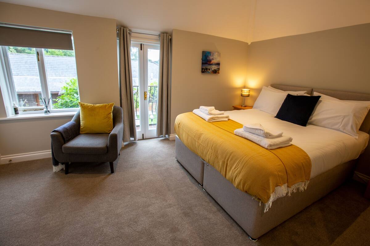 A hotel room with a bed, a chair, a nightstand, a lamp, and a window with curtains.