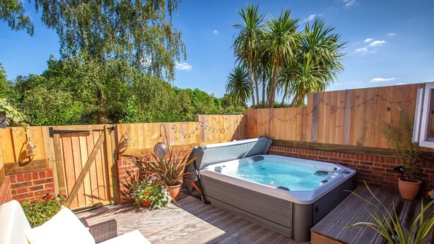 A wooden deck with a hot tub, outdoor furniture, and a wooden fence. - The Three Lions (Fordingbridge)
