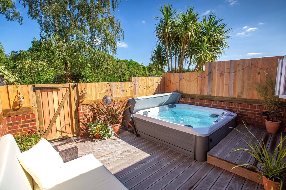 A wooden deck with a hot tub, outdoor furniture, and a wooden fence.