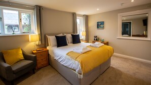 A neatly arranged bedroom with a bed, bedside tables, a chair, and a large mirror. - The Three Lions (Fordingbridge)