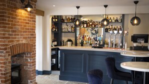 A bar area with a brick fireplace, shelves of liquor bottles, and a coffee machine. - The Three Lions (Fordingbridge)