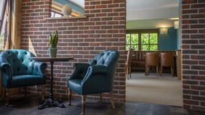 A room with brick walls, two green leather armchairs, a small table with a potted plant, and a wooden ceiling beam. - The Three Lions (Fordingbridge)